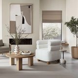 A modern living room showcases a LuxenHome Tia ivory barrel accent chair with wood ball legs, a round wooden coffee table with snacks, and a large abstract painting. A tall plant adorns the corner, while a window with beige blinds lets in natural light, creating a calm atmosphere with neutral tones.