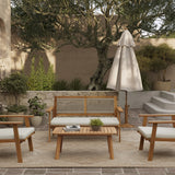Outdoor patio featuring an outdoor loveseat set crafted from FSC-certified Acacia wood, accompanied by chairs, a sofa, and a table. A closed umbrella shades potted plants and a large tree in the background on a stone surface.