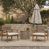 Two FSC-certified wooden chairs with cushions, featuring a rope back design, accompany a round table and parasol on the carpeted outdoor patio. A stone wall and trees create a serene backdrop.