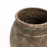 A close-up of a weathered, round terracotta urn vase with a wide, open top showcases its textured surface and earthy tones against a white background. This rustic piece is perfect for both indoor and outdoor settings.