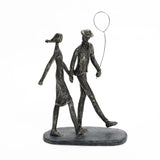 A modern resin home decoration, this stylized sculpture features two figures walking gracefully, one gently holding a balloon.