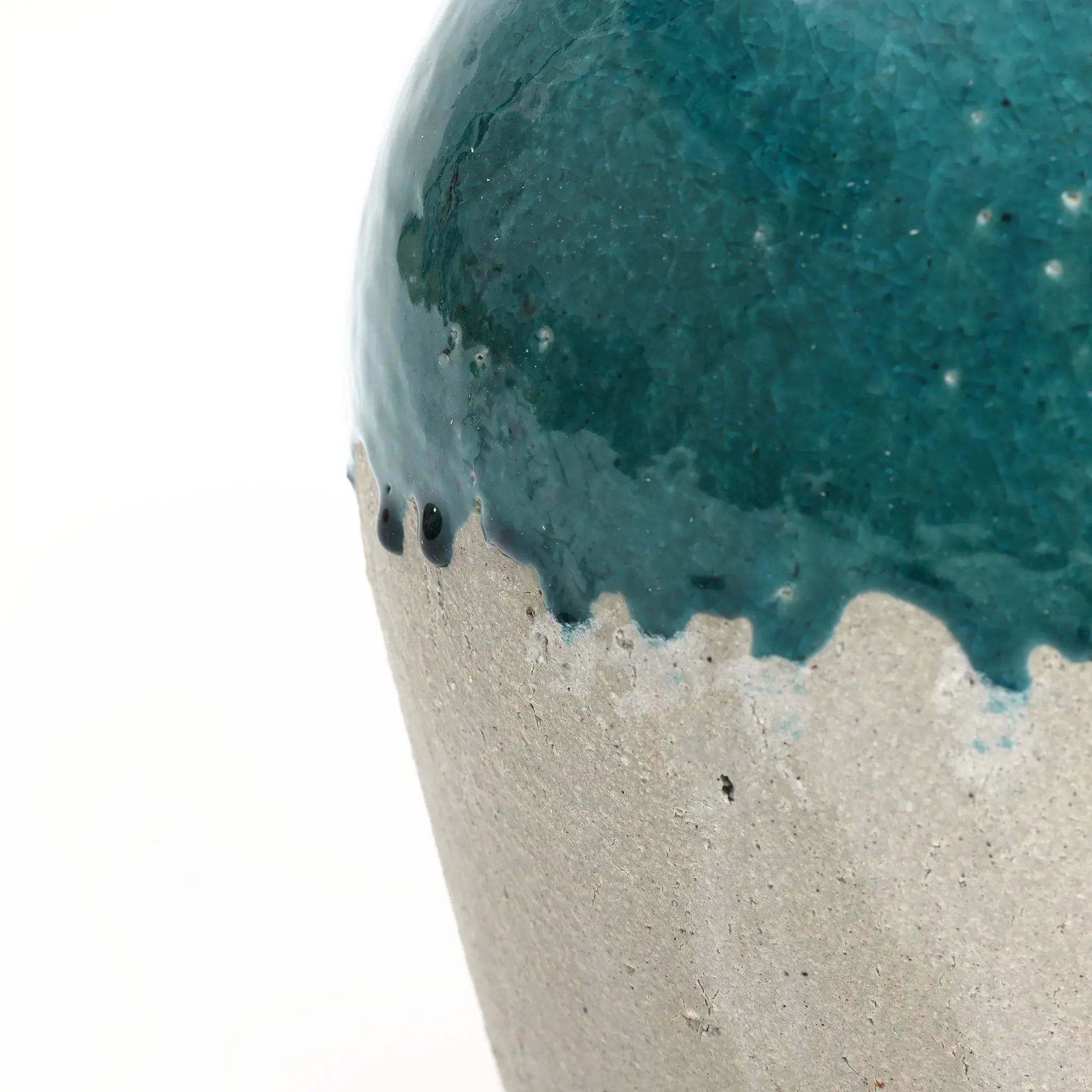 Close-up of a ceramic vase showcasing rustic design with a textured, glossy teal glaze on the upper section and a rough, matte gray surface below. Suitable as an indoor and outdoor jar vase, it adds charm to any setting with its artisanal appeal.