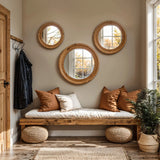 A cozy entryway features a wooden bench with brown cushions and woven ottomans. Three rubberwood framed mirrors create an optical illusion on the wall, while a coat hangs on a wooden hook. Sunlight streams through large windows, adding warmth to this inviting space.