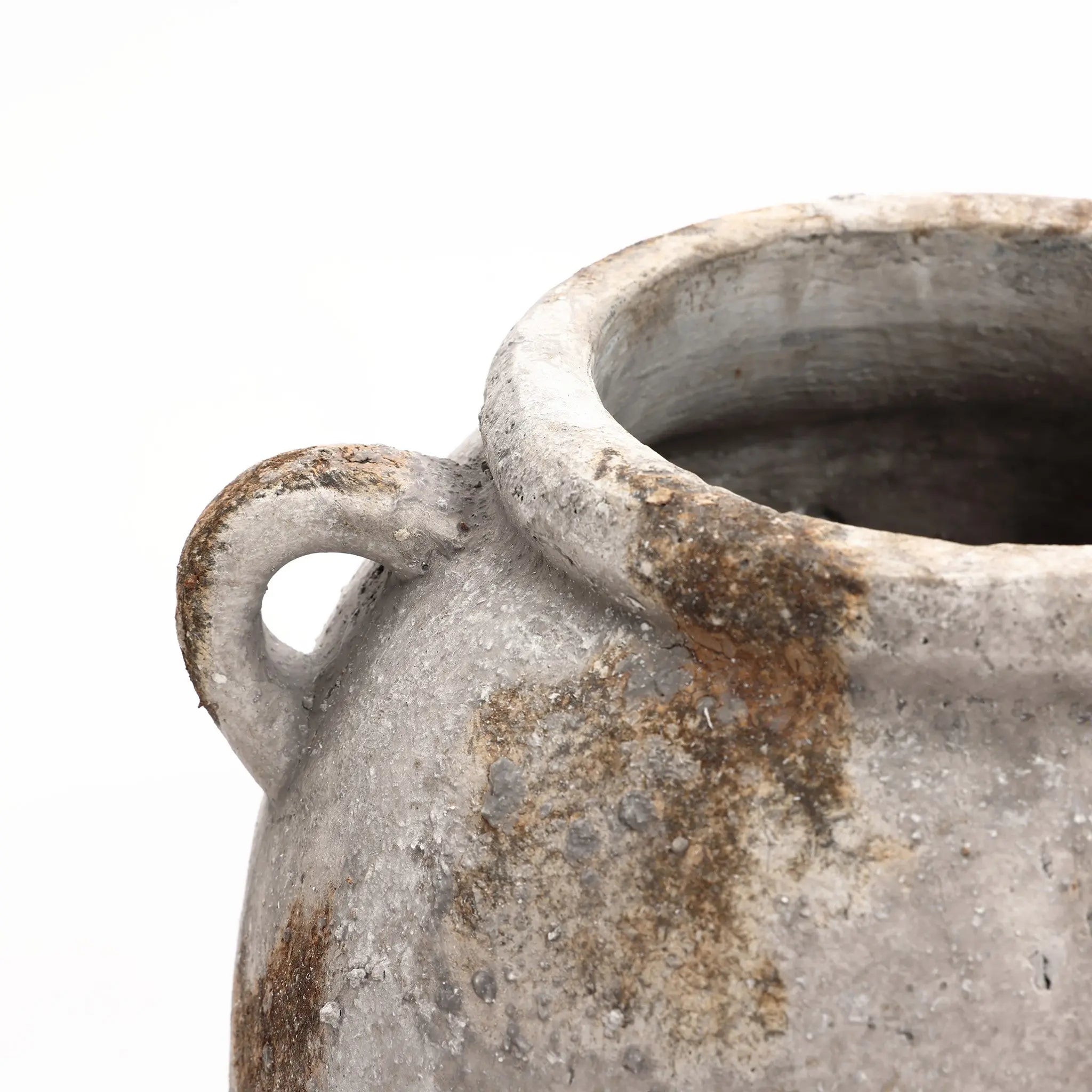 Close-up view of a handcrafted, weathered ceramic pot with a rounded shape and small loop handle on a white background, exuding vintage appeal.