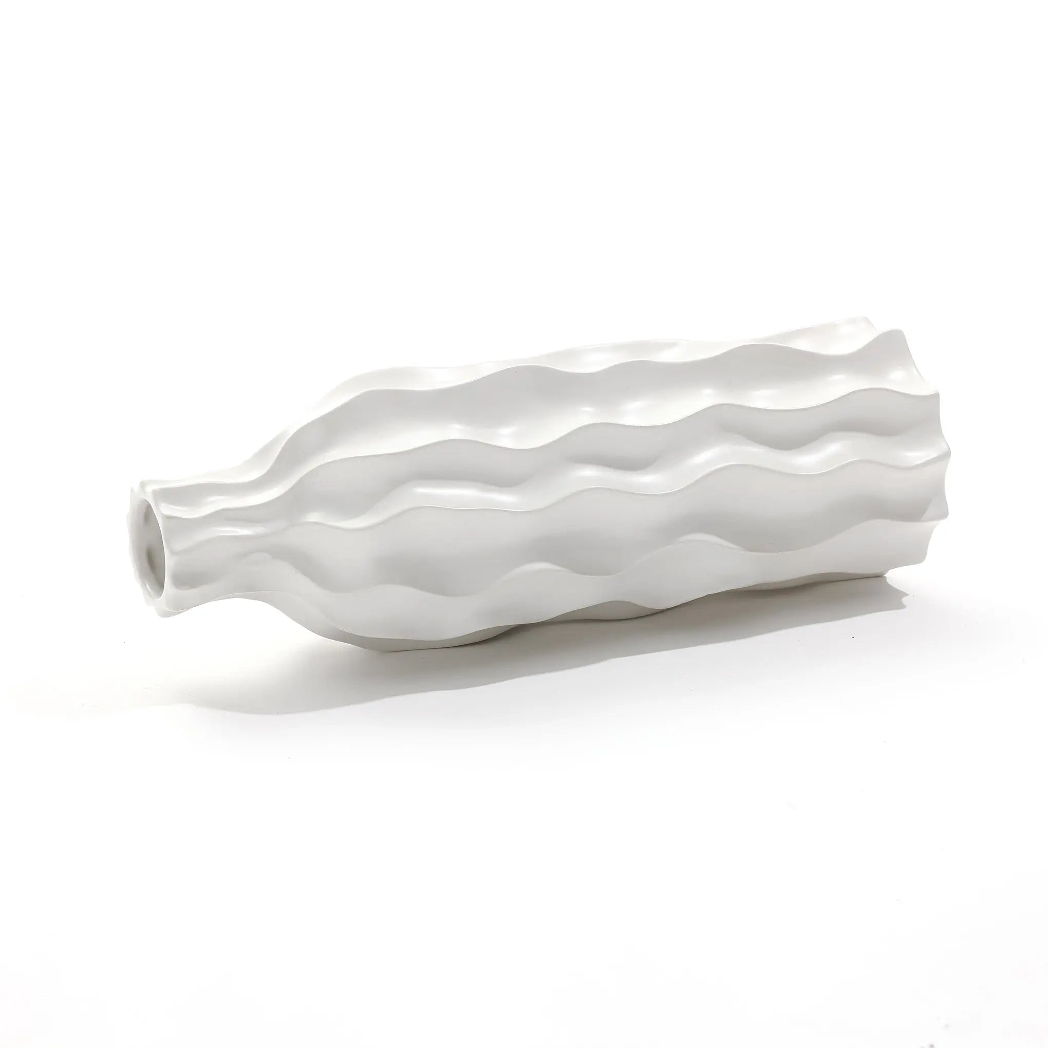 An elegant ceramic vase with a wavy, textured design lies gracefully on its side against a plain background, showcasing its versatile charm.