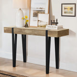 A modern farmhouse console table with black legs and an oak finish features a white lamp, yellow flowers in a vase, two framed pictures, books, and a small candle holder, all set against a crisp white wall.