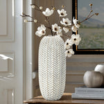 LuxenHomes Modern geometric pattern resin tall vase, 17 h, with an antique effect and white blossoms, stands on a wooden table beside two round vases. Its set against a cozy interior backdrop showcasing a partially visible painting.
