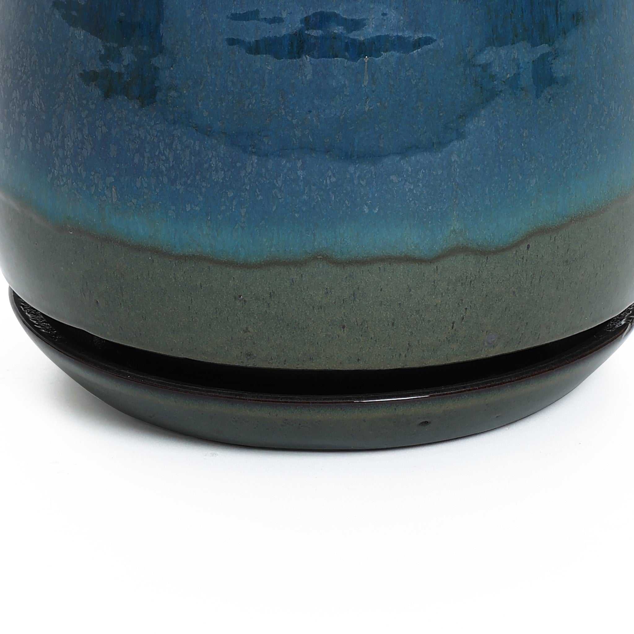 A close-up of a decorative ceramic planter featuring a gradient of dark green to blue glaze, complete with drainage holes and a matching base.
