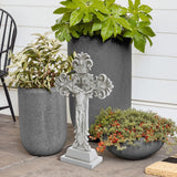 A decorative stone cross stands gracefully beside three potted plants on the patio, with a serene white wall framing the scene. This charming arrangement subtly echoes the Christian faith, inviting peace and reflection in its simplicity.