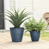 Two blue decorative planters sit on a wooden deck, each with unique charm: one boasts a tall spiky plant while the other cradles a leafy fern, offering vibrant contrast against the white house. These pots feature UV-protected finishes for lasting beauty in both indoor and outdoor use.
