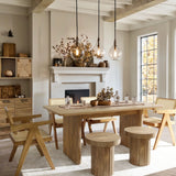 The dining room showcases a LuxenHome Aria wood finish 63 wide rectangle dining table with matching chairs and stools. Three pendant lights illuminate the spacious tabletop, complemented by a decorated mantel with vases and a window view of autumn leaves, creating a warm, rustic interior.