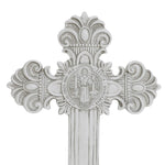 Silver decorative cross with ornate flourishes and an embossed image of a saint at the center, surrounded by inscriptions, perfect for celebrating religious occasions.