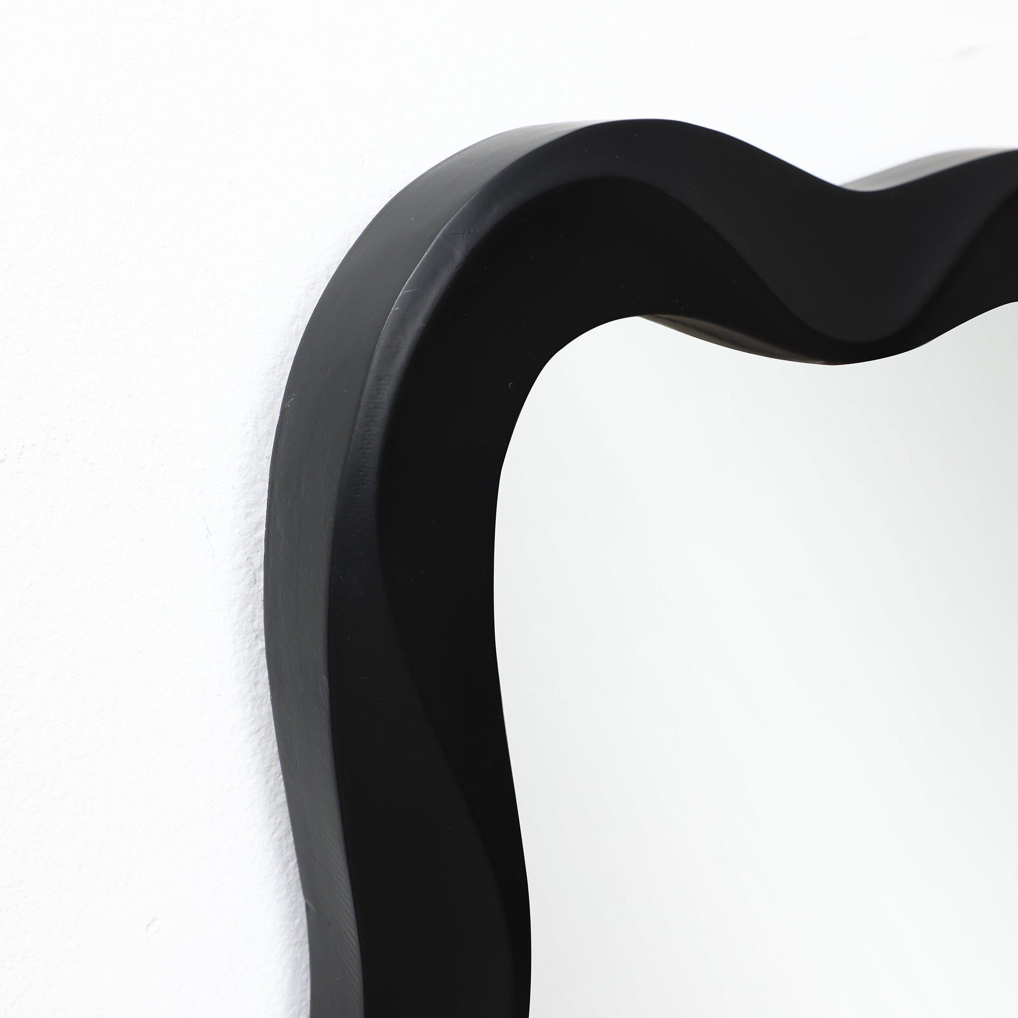 Close-up of the top left corner of a frame mirror with a thick black border, creating a striking contrast against.