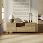 Light walnut-colored wood defines this wooden sideboard, topped with a lamp, books, and candlesticks. A textured wall art piece hangs above, adding to the mid-century modern charm. The room is bright with natural light and offers a glimpse of the adjoining living space.
