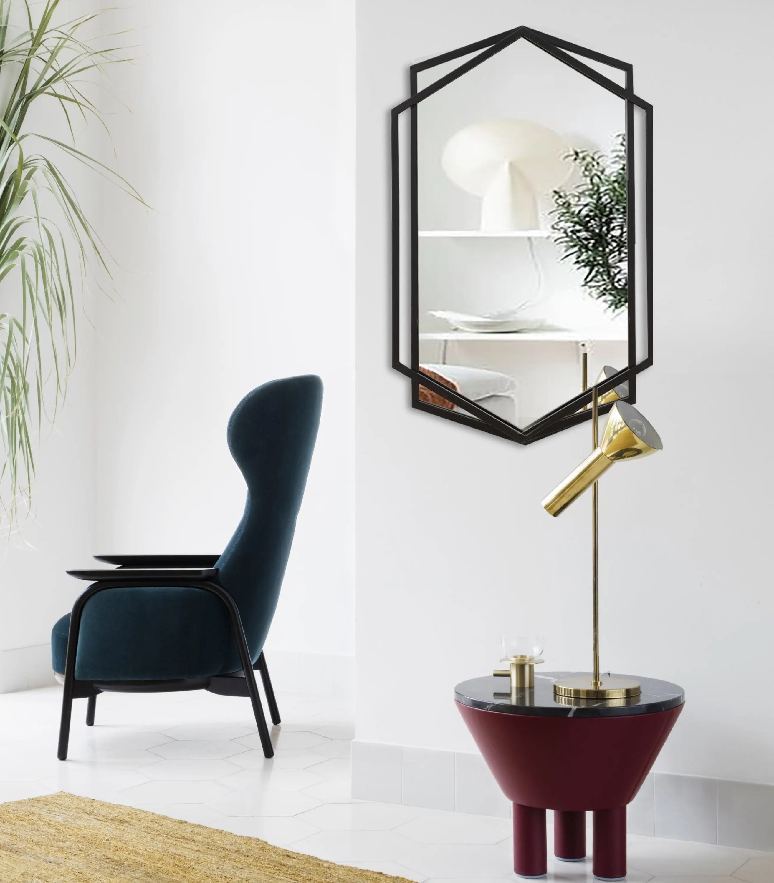 A modern living space with a black armchair, a gold lamp on a maroon round table, a hexagon shape black wall mirror, and a large green plant.