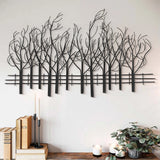 Contemporary style wall decoration featuring metal wall art of leafless trees above a shelf with candles, books, and a potted plant on a light-colored wall adds elegant nature theme wall decor to any space.