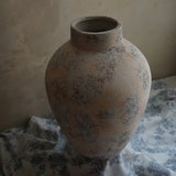 A large, textured ceramic vase enhances the floral-patterned fabric backdrop against a light wall with a subtle white marble texture, creating an elegant home decor statement.