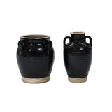 Two handcrafted black ceramic pots, finished with a smooth glaze, sit side by side against a plain white background. Their wide bases and small handles add to their simple elegance.