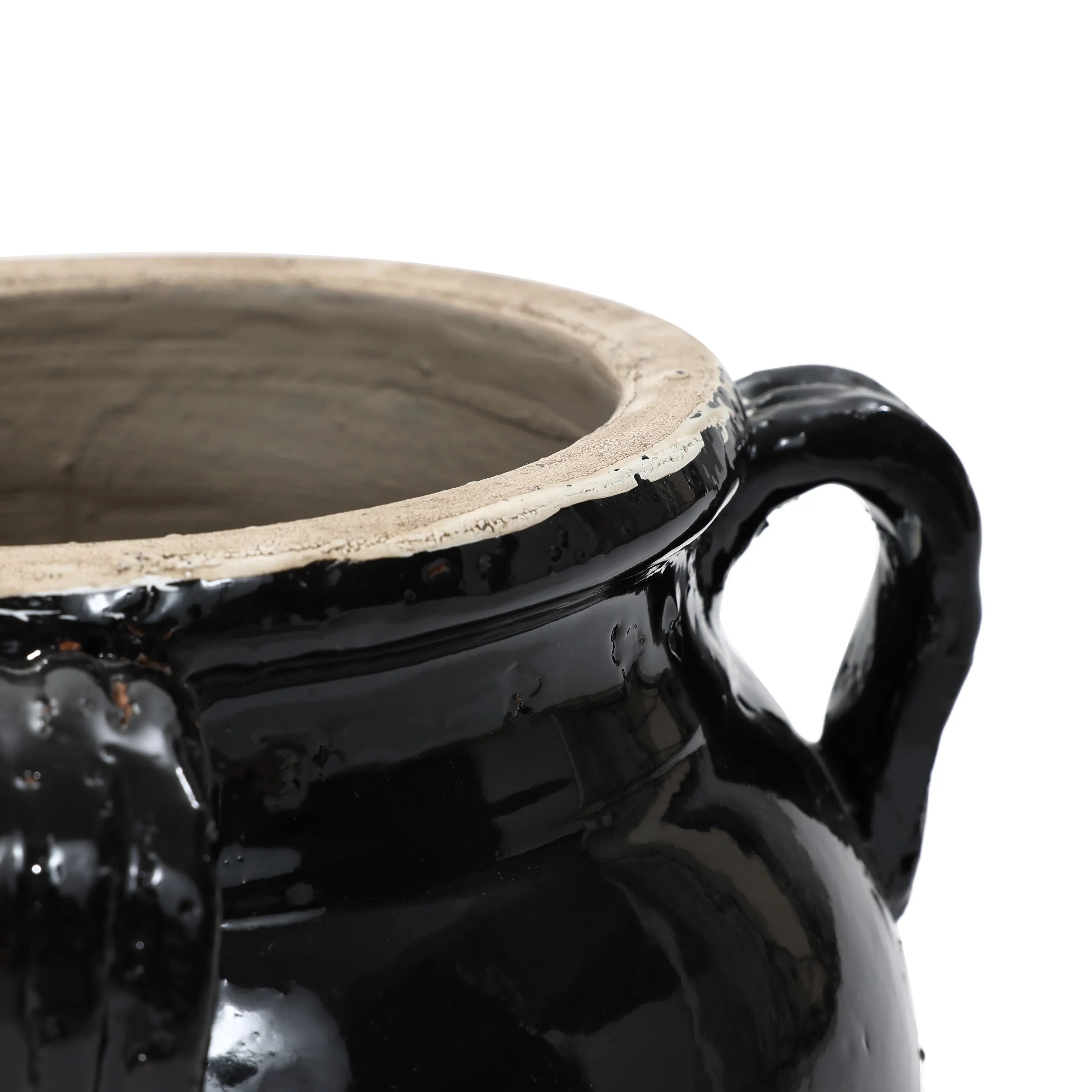 Close-up of a glossy black glazed ceramic pot with two handles and a beige interior rim, showcasing its handcrafted elegance.