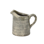 A textured, old-fashioned ceramic pitcher vase with a handle and a spout, showcasing artisanal craftsmanship and a worn, rustic terracotta finish.