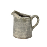 A textured, old-fashioned ceramic pitcher vase with a handle and a spout, showcasing artisanal craftsmanship and a worn, rustic terracotta finish.