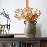 A handcrafted ceramic vase adorned with autumn leaves sits on a wooden shelf, accompanied by a black metal deer sculpture. Below, books add their own historic depth to the scene.