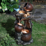 Three rustic pots create a tiered outdoor fountain with LED lights, nestled among grass and plants; a blue bird figurine perches atop the highest pot.