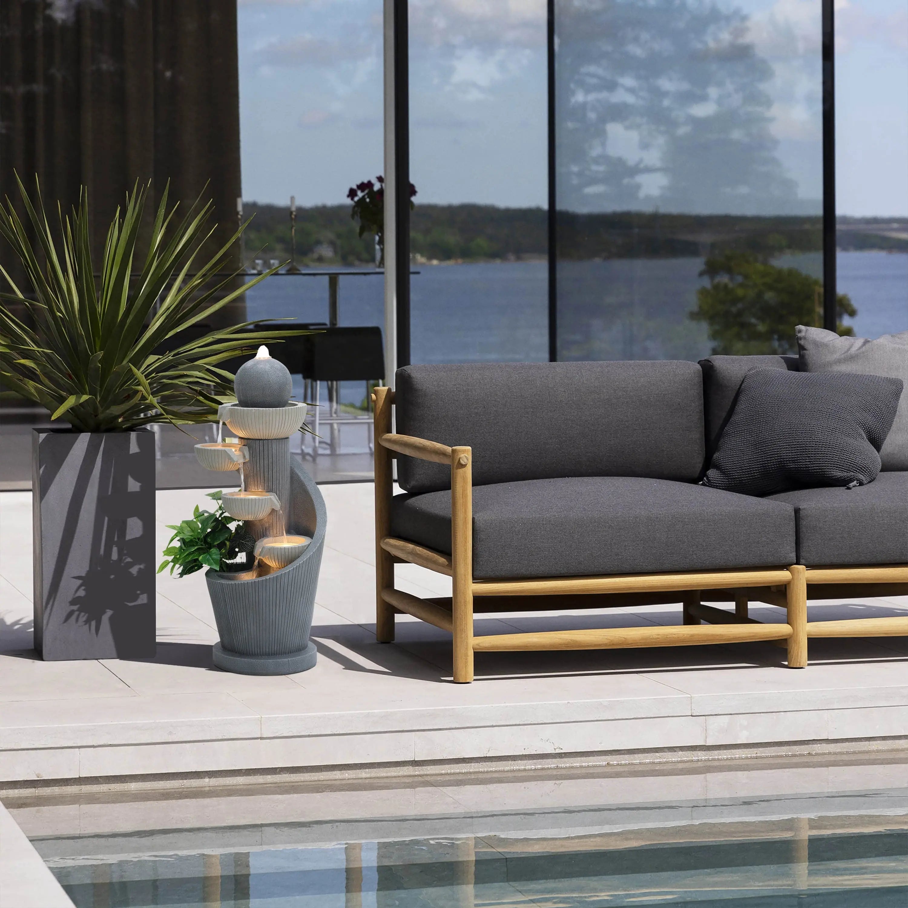 grey-cement-outdoor-fountain-standing-in-front-of-swimming-pool-in backyard
