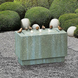 A rectangular stone birdbath with six small bird sculptures on its edges serves as a charming outdoor fountain, set in a gravel garden with trimmed green bushes and large round stones in the background.