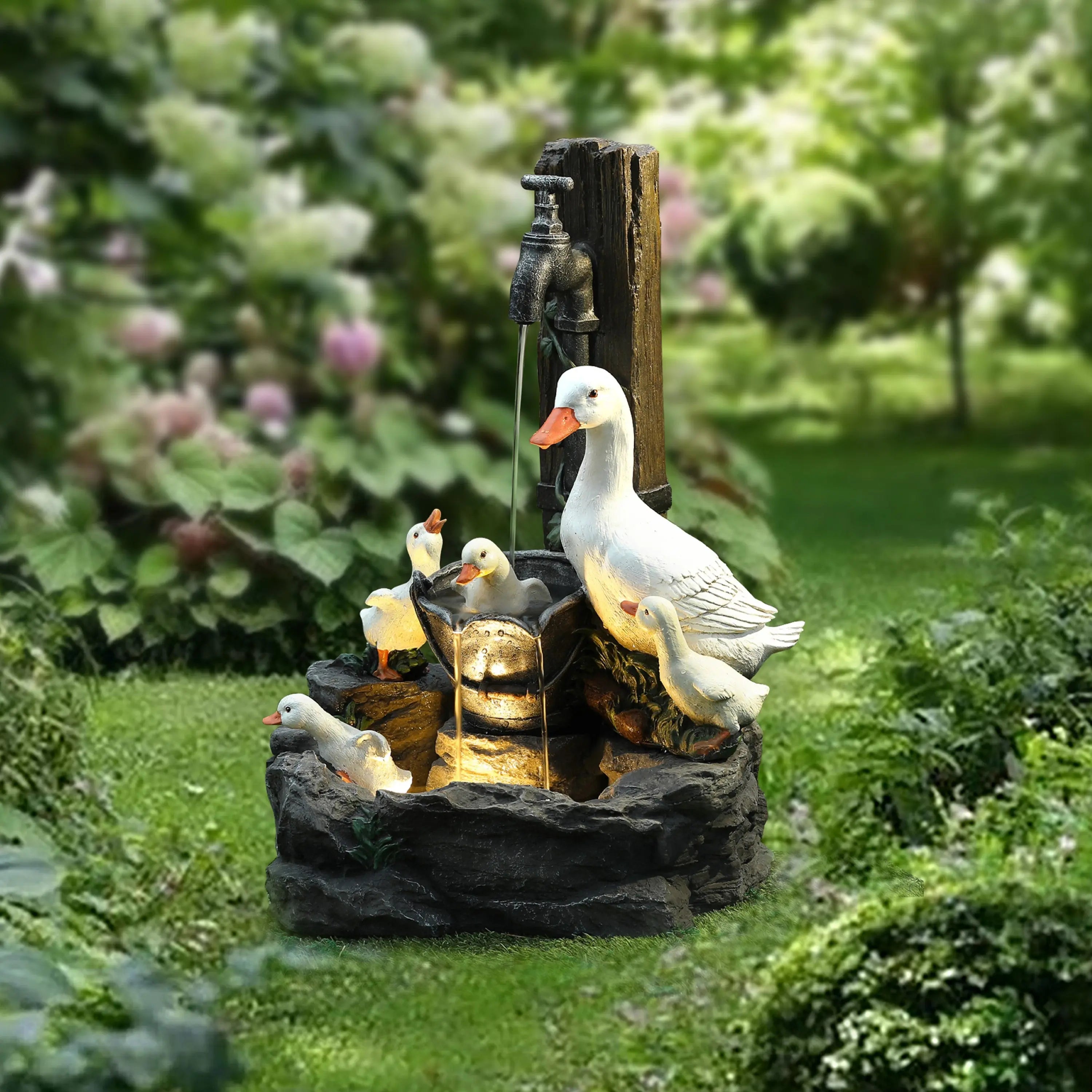 Outdoor garden scene featuring a resin water fountain with a goose and goslings, a water spout illuminated by an LED light, and surrounding greenery and flowers to enhance your outdoor space.