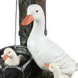 A close-up of three white duck statues, including one standing duck and two ducklings, with one sitting in a resin water fountain with water flowing—perfect for brightening any outdoor space.