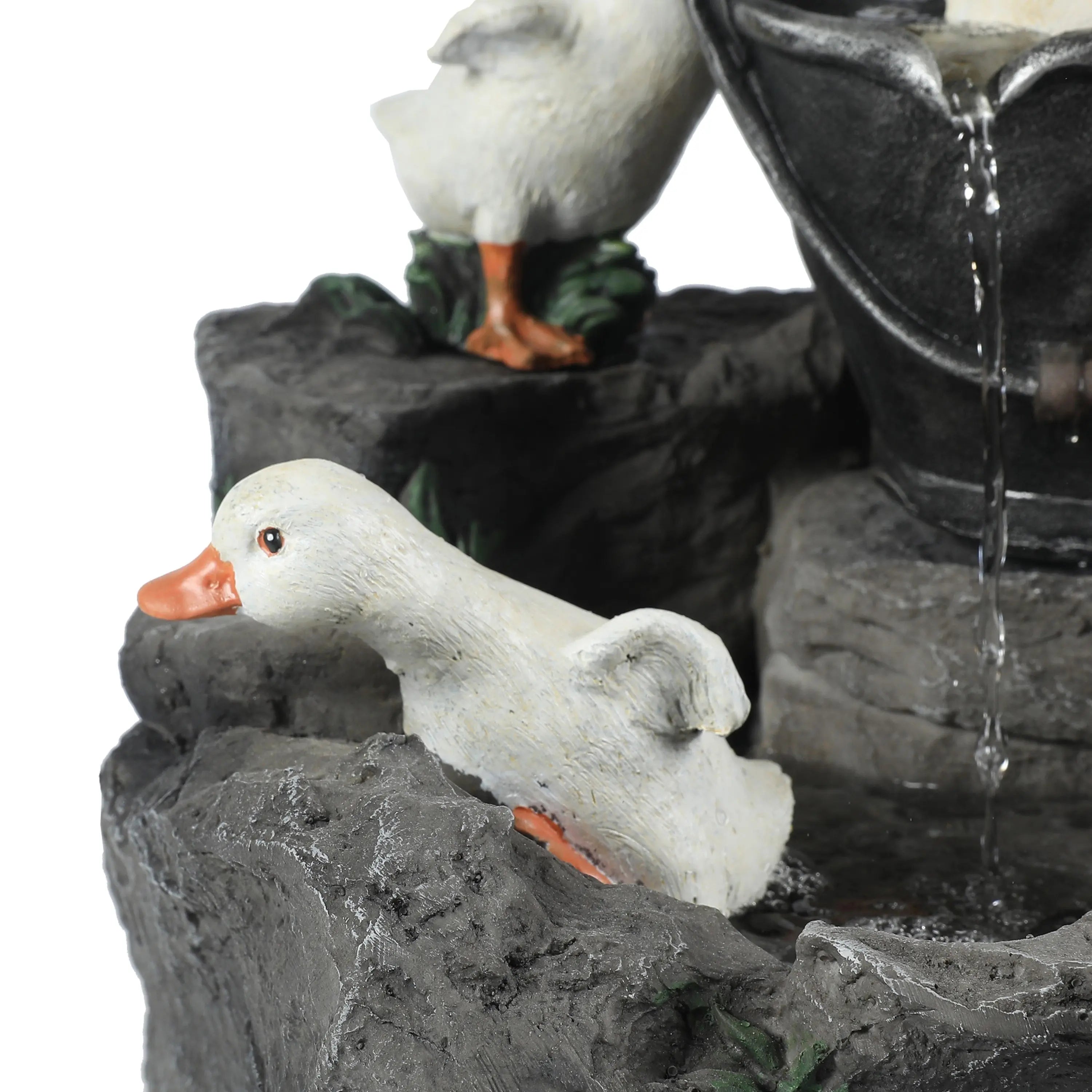 A white duck figurine with an orange beak and feet sits on gray textured rocks near a small waterfall feature, adding charm to any outdoor space.