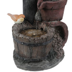 A small bird figurine sits on the rim of a rustic wooden bucket, with water trickling in from an upper spout, adding vintage farmhouse décor and rustic charm to any space.