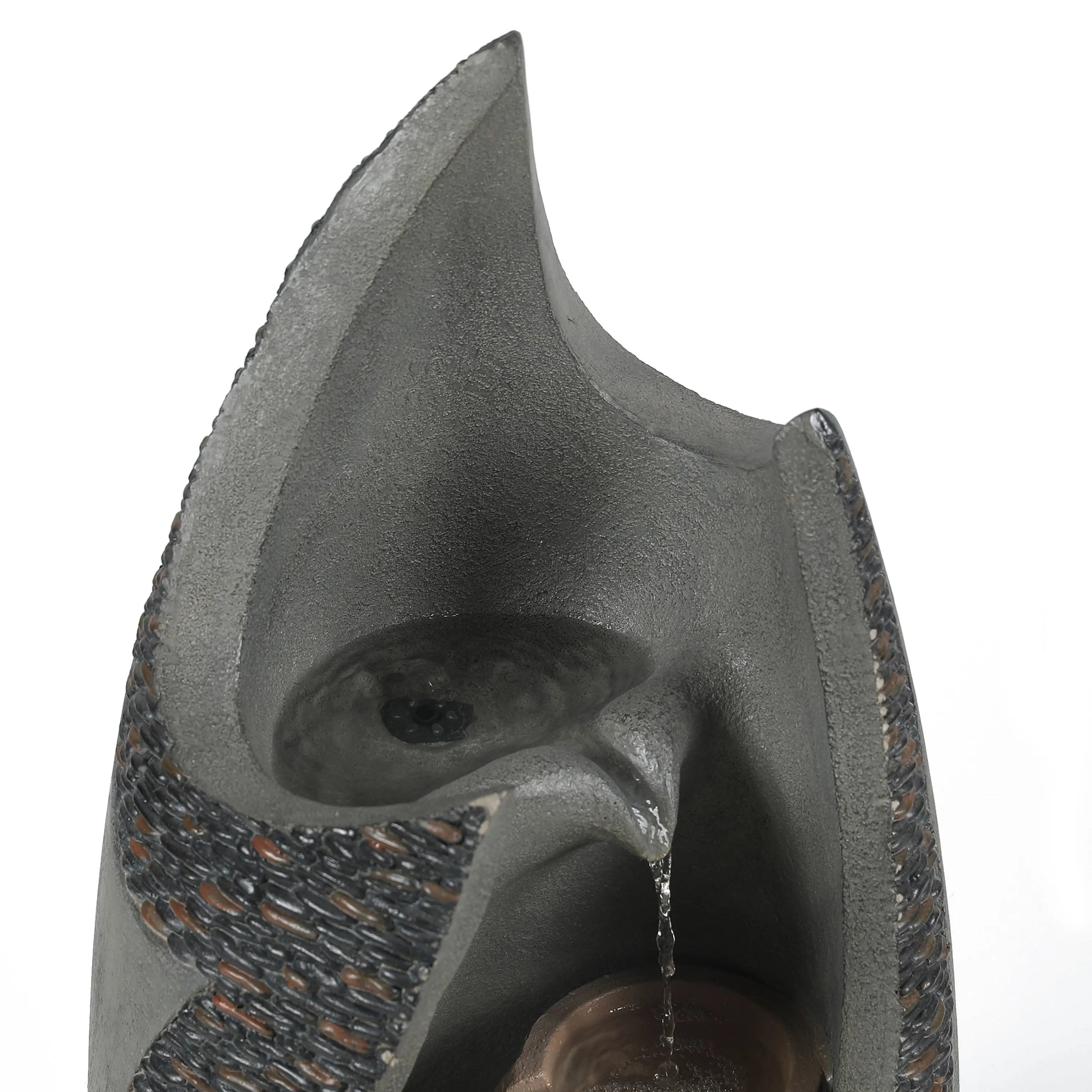 Close-up of a modern patio fountain with a cascading curved structure and textured surfaces, showing water flowing from an upper basin into a lower one against a white background.