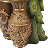 A decorative gold vase with ornate patterns stands next to green peacock feathers with blue and orange eye spots, creating a striking garden décor display.