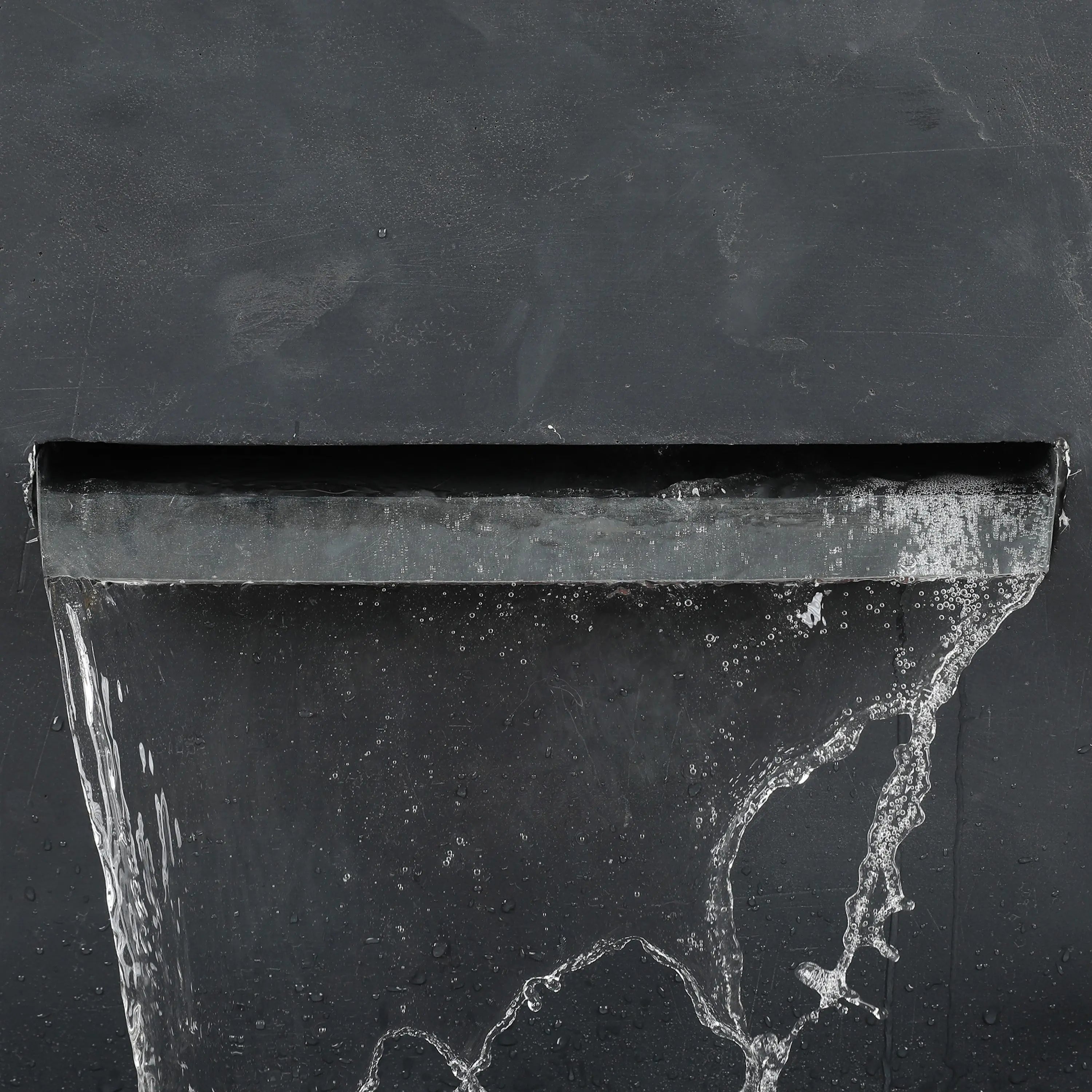 A close-up of water flowing from a modern gray rectangular spout against a dark, textured wall, capturing the elegance of a waterfall outdoor fountain.