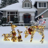 Three Deer Family Decorations with lights and red bows stand on a snowy lawn in front of a house adorned for winter, with an LED Holiday Decor snowman inflatable by the porch.