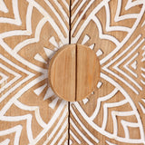 Close-up of a round wooden cabinet knob on accent cabinet doors, featuring a natural wood finish with white geometric patterns and intricate floral scroll work.