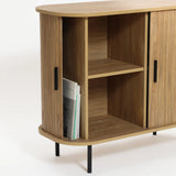 Mid-Century Modern Accent Cabinet featuring an oak grain finish and black handles, this wooden cabinet boasts open shelves with magazines stored vertically in the left shelf. Slatted tambour doors add a stylish touch to its design.