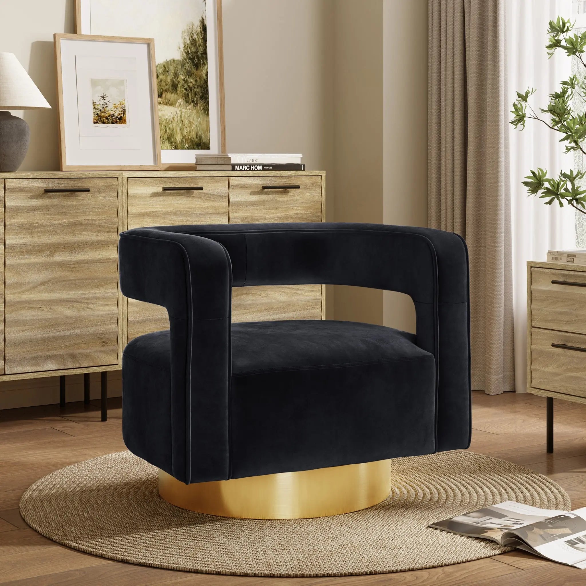 A modern accent chair with a black velvet finish and curved backrest on a gold base offers 360-degree rotation, sitting elegantly on a round beige rug. In the background, wooden cabinets, framed art, and a potted plant complete the stylish scene.