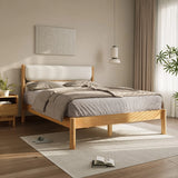 A neatly made bed with grey sheets and a luxurious white boucle fabric cushioned headboard exudes modern sophistication in a bedroom with wooden floors. A bedside table holds plants, an open book, shoes, and a hanging lamp gracefully illuminates this serene sanctuary.