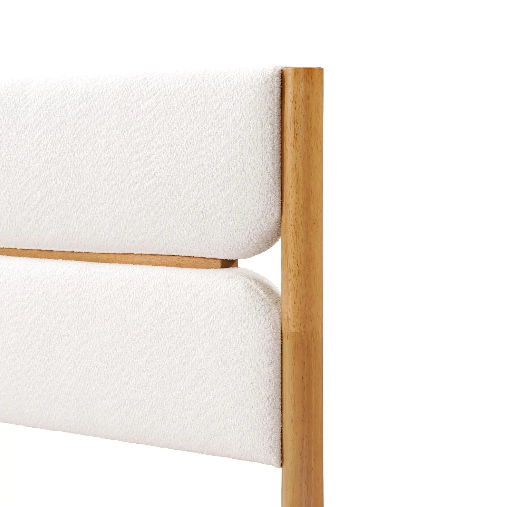 A corner of a solid wood bed features a wooden-framed headboard with padded, luxurious white boucle fabric, exuding modern sophistication.
