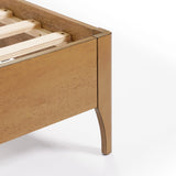 Close-up of a contemporary Rubberwood Platform Bed featuring a wooden frame corner with slats. The light brown finish and simple, modern design elegantly complement an upholstered headboard, enhancing its visual dimension.