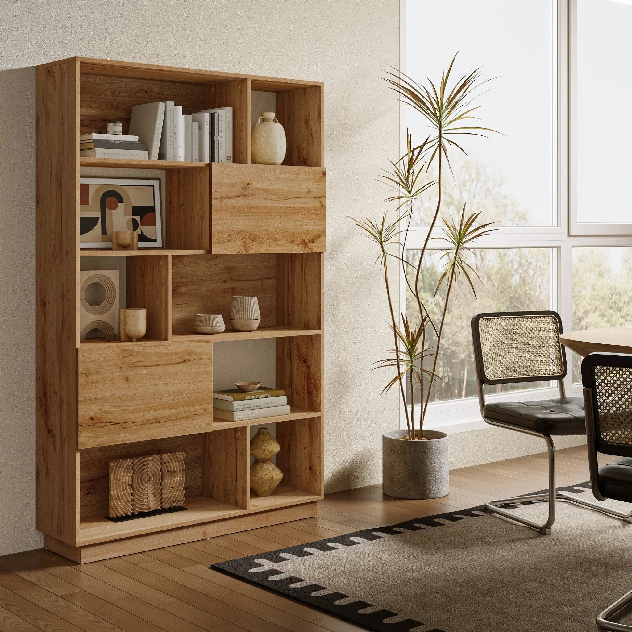A modern-style bookshelf with ample storage, adorned with books and decorative items, stands beside a potted plant. Crafted in a light walnut finish, it complements two nearby chairs and a table as sunlight streams through the window.