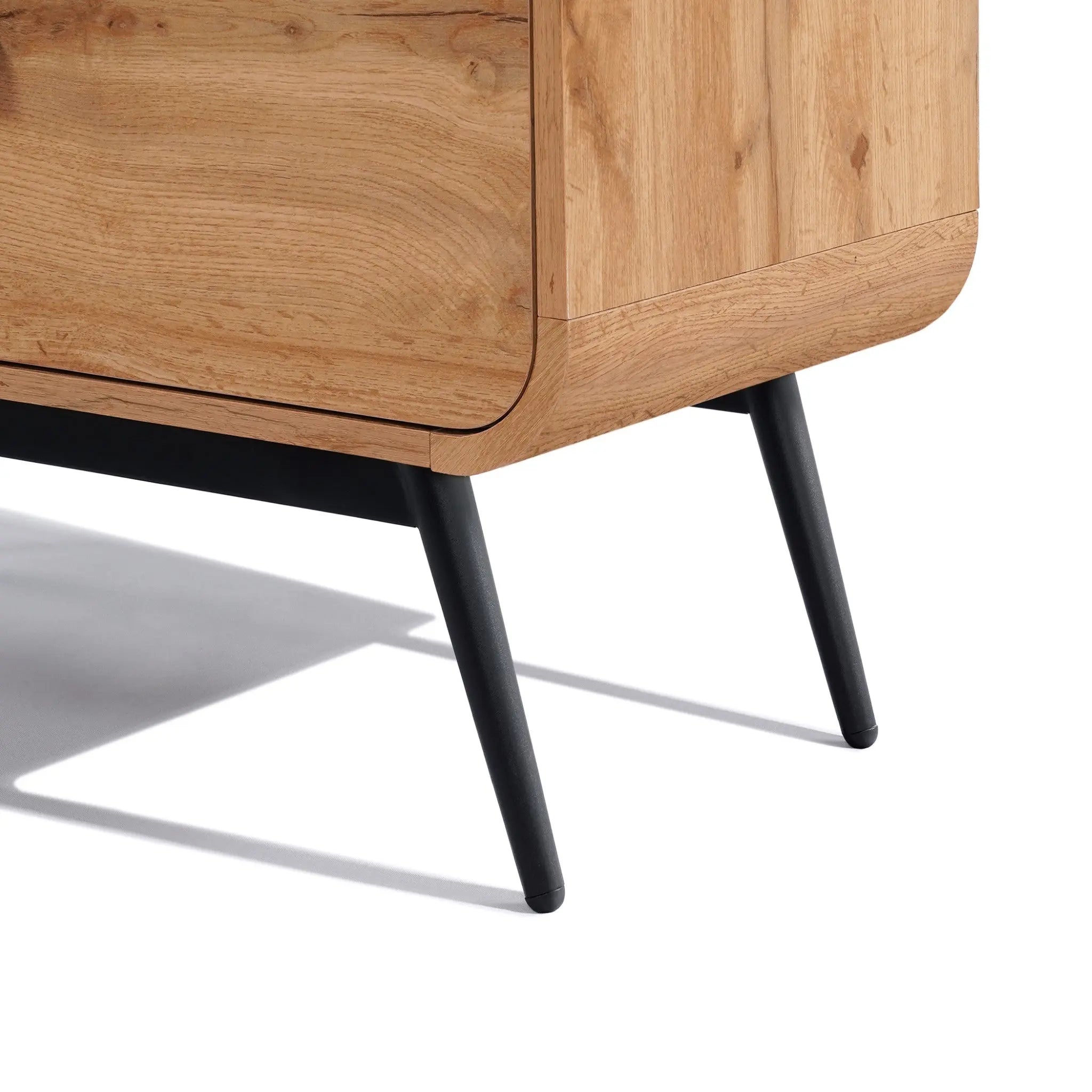 Close-up of a freestanding cabinet corner with smooth edges and black angled legs, showcasing a walnut oak finish and capturing the essence of mid-century modernism against a white background.