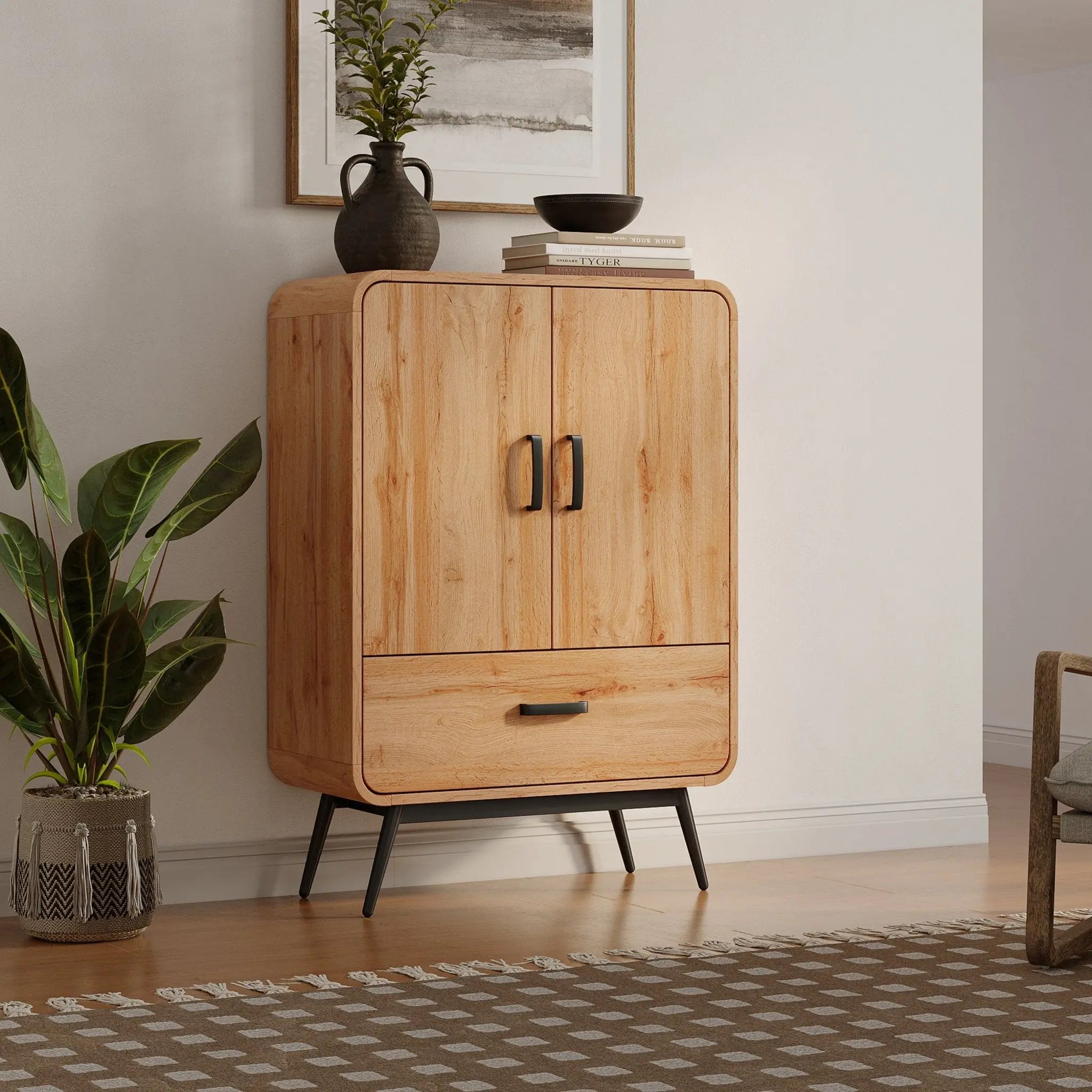 The freestanding wooden cabinet, boasting a walnut oak finish and metal handles, features two doors and one drawer. Its perfectly placed in a room with a potted plant, a rug, and wall art above, exuding an air of mid-century modernism.