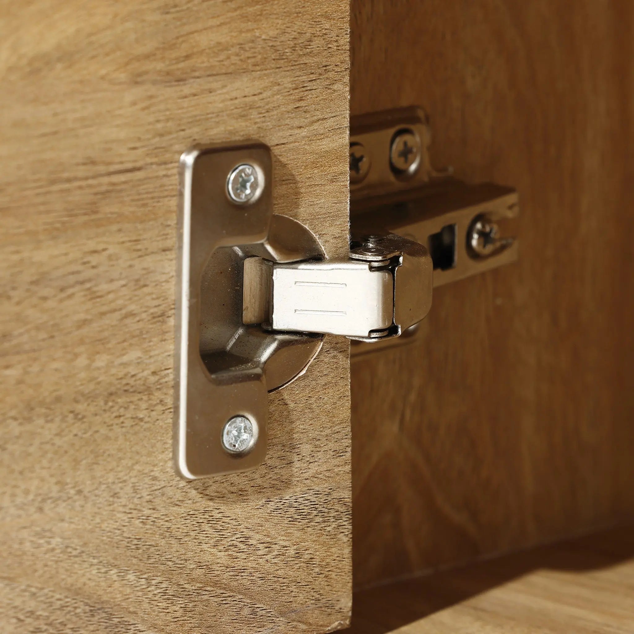Close-up of a metal hinge on a wooden cabinet door, partially open, revealing the light walnut-colored wood that embodies a mid-century modern charm.