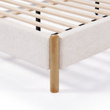 Close-up of a beige fabric bed frame featuring a queen-sized white boucle headboard and a wooden leg with a slatted base.