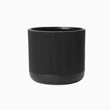 A black, cylindrical planter featuring a subtle stripes pattern and a ribbed texture crafted from magnesium oxide material on a white background.