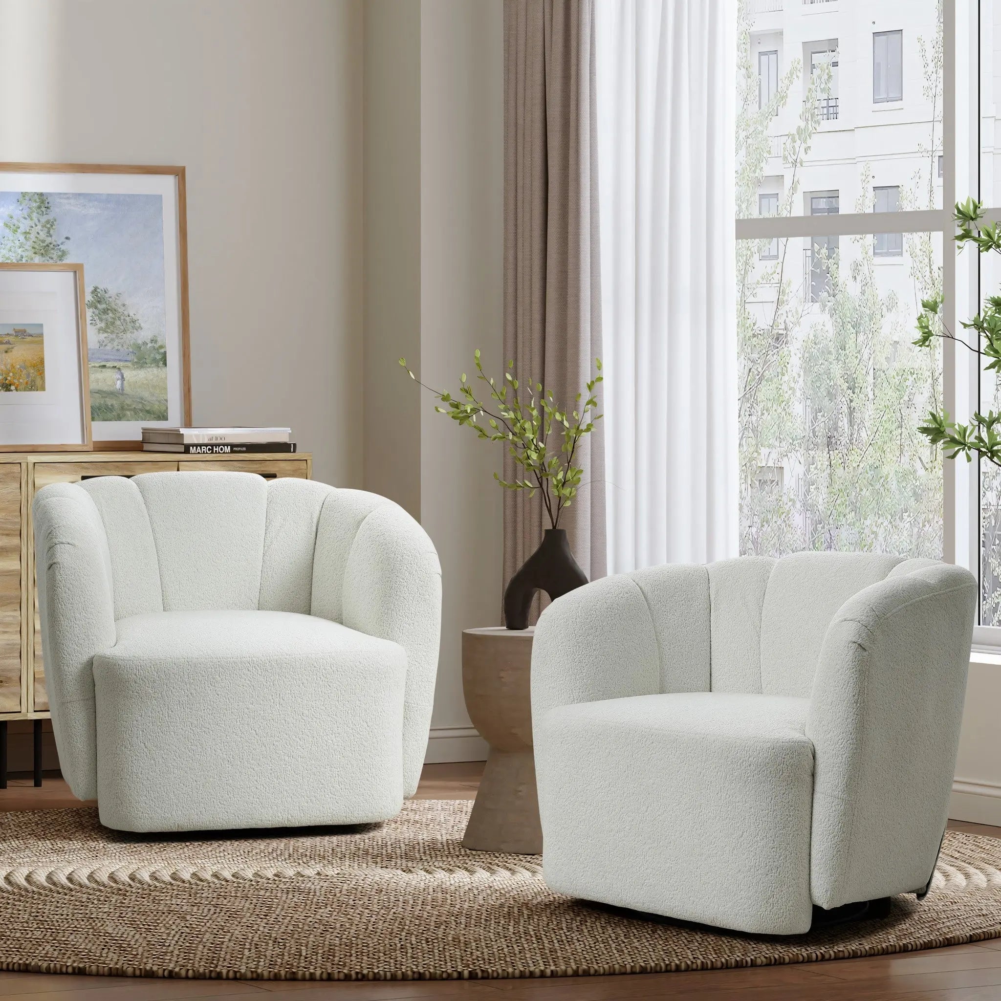 A cozy living room showcases a LuxenHome Amber ivory boucle swivel barrel accent chair and another upholstered chair on a round woven rug. Between them is a small wooden side table with a vase. Natural light through sheer curtains highlights framed art on a wooden cabinet in the background.